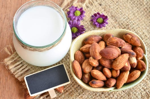 Almond milk in glass with almonds and blank tag on sack background.