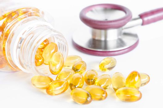 Fish oil capsules spilling out of a bottle and stethoscope on white background.