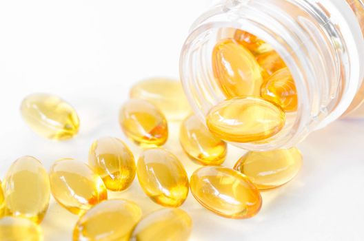Fish oil capsules spilling out of a bottle on white background.