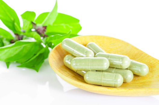 Green Herb capsule on wooden spoon and leaf on white background.