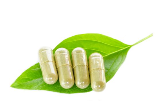 Yellow herb capsule with green leaf on white background.