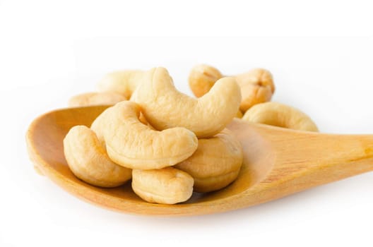 Cashew nuts with salt in wooden spoon on white background.