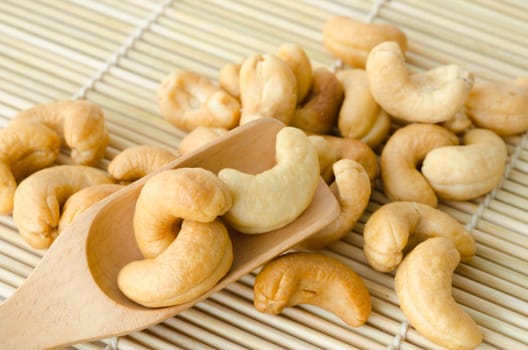 Cashew nuts with salt in wooden spoon on mat background.