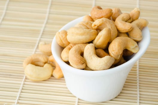 Cashew nuts with salt in white bowl on mat wooden background.
