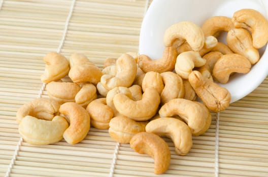 cashew nuts with salt in white cup on wooden mat.