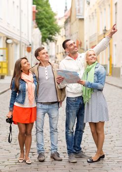 travel, vacation, technology and friendship concept - group of smiling friends with map and photocamera exploring city