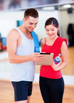 fitness, sport, training, technology and lifestyle concept - two smiling people with tablet pc computer and water bottle in the gym