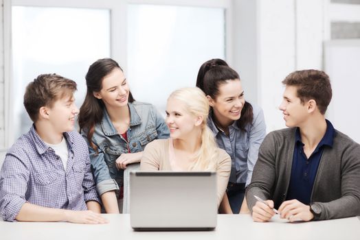 education, technology and internet concept - smiling students with laptop at school looking at each other