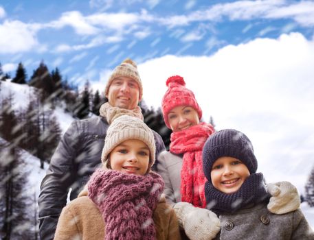 family, childhood, season and people concept - happy family in winter clothes over snowy mountains background