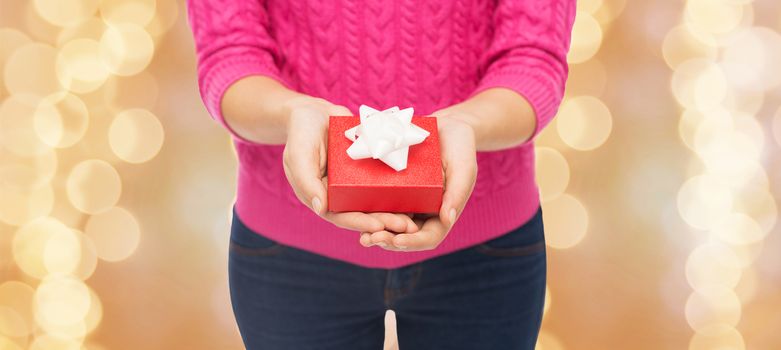 christmas, holidays and people concept - close up of woman in pink sweater holding gift box over beige lights background