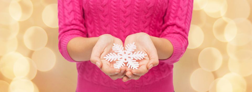 christmas, holidays and people concept - close up of woman in pink sweater holding snowflake over beige lights background