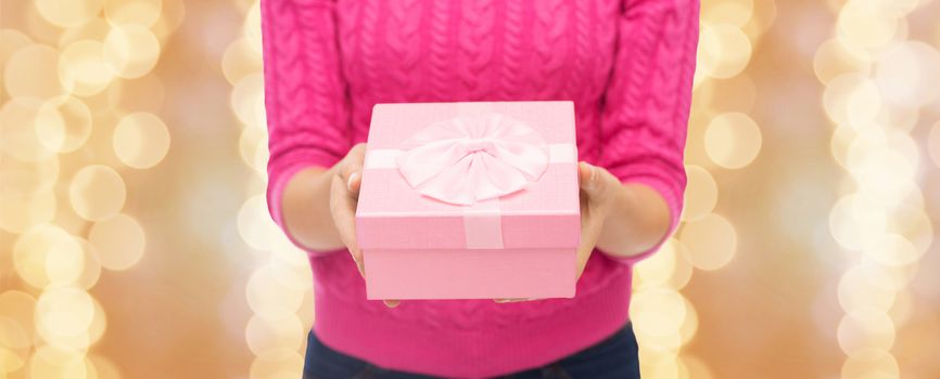 christmas, holidays and people concept - close up of woman in pink sweater holding gift box over beige lights background