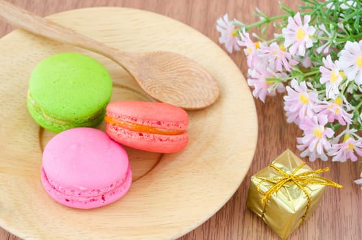 Colorful macaroons in wooden dish and flower on wooden background.