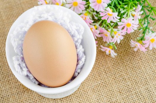 Egg in white bowl and flower on sack background.
