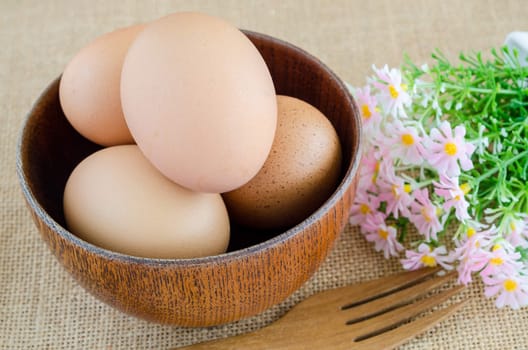 Brown eggs in wooden bowl and flower on sack background.