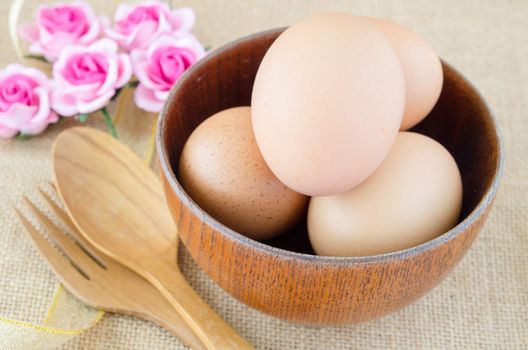 Eggs in wooden cup and wooden spoon on sack background.