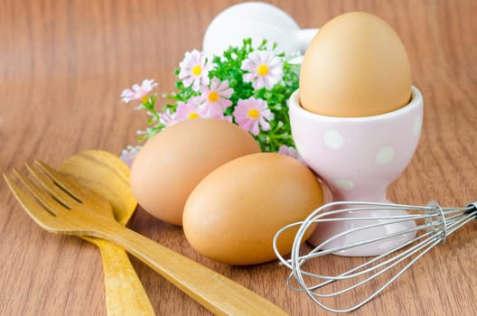 Eggs in bowl and wooden spoon with flower on wooden background.