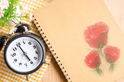 Clock diary brown color with red rose on wooden. Vintage style background.