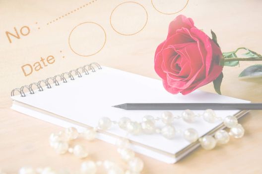 Red rose and open white diary with black pencil on diary background.