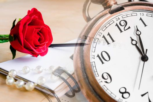 Red Rose and a pocket watch with diary on wooden background.