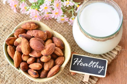 Almonds in cup and almond milk in glass with healthy tag on sack background.