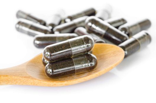 Black herbal capsule drug in wooden spoon on white background.