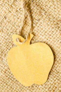Brown blank tag apple shape on sack background. Recycle paper concept.