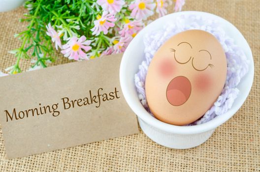 Morning breakfast tag. Eggs sleep with Expression Face in white cup and flower on sack background.