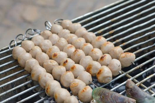 Meatballs on metal skewers being grilled on a barbecue