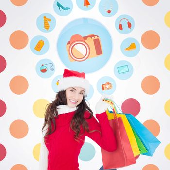 Festive brunette in winter wear holding shopping bags against colorful polka dot pattern 