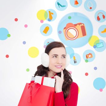 Brunette with ear muffs holding shopping bag full of gifts against dot pattern