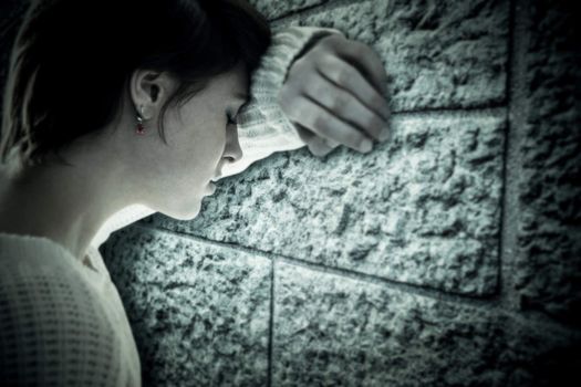 Sad pretty brunette leaning against wall against grey brick wall