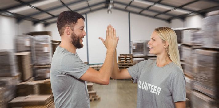 Smiling volunteer doing high five in office against many stack of cardboard boxes