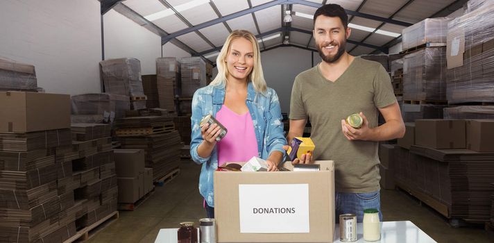 Portrait of happy colleagues smiling while holding products  against forklift in a large warehouse