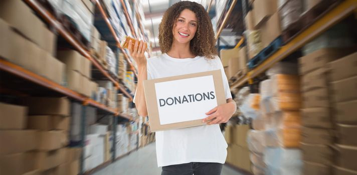 Happy volunteer holding a box of donations and jam jar against shelves with boxes in warehouse