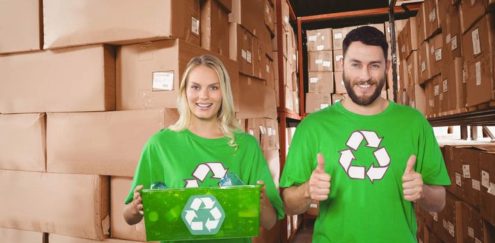 Portrait of cheerful volunteers in recycling symbol tshirts  against shelves with boxes in warehouse