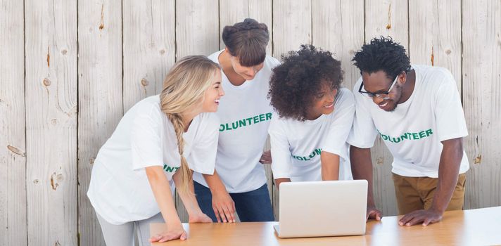 Smiling volunteers working together on a laptop against wooden background