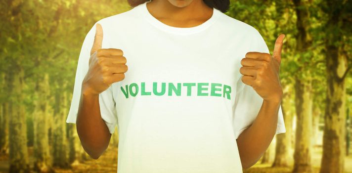 Woman wearing volunteer tshirt and giving thumbs up against walkway along lined trees in the park