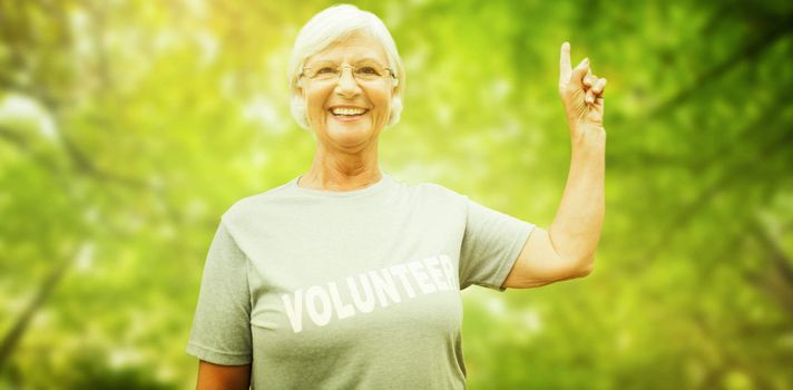 Happy volunteer grandmother with thumbs up  against green leaves