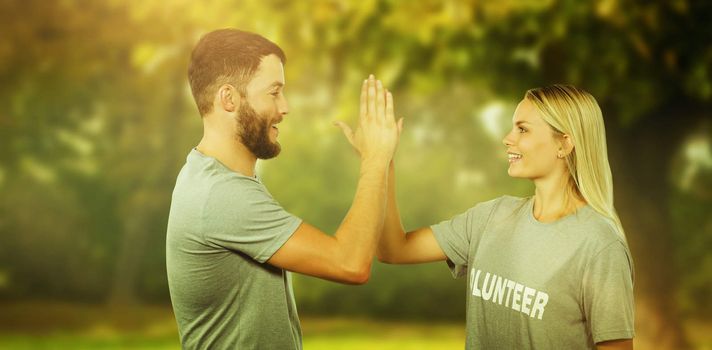 Smiling volunteer doing high five in office against trees and meadow in the park