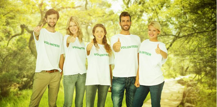 Group portrait of happy volunteers gesturing thumbs up against wooden trail across countryside