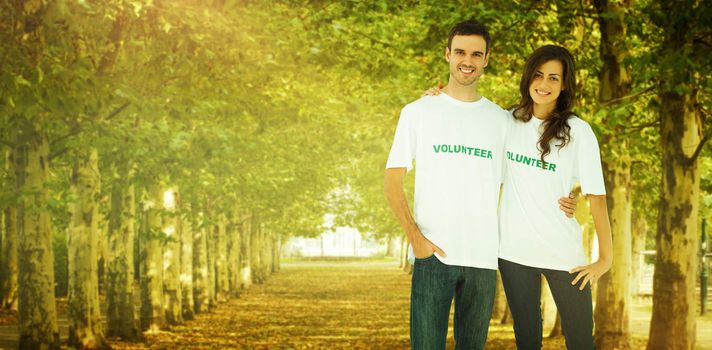 Two cheerful people wearing volunteer tshirt against walkway along lined trees in the park