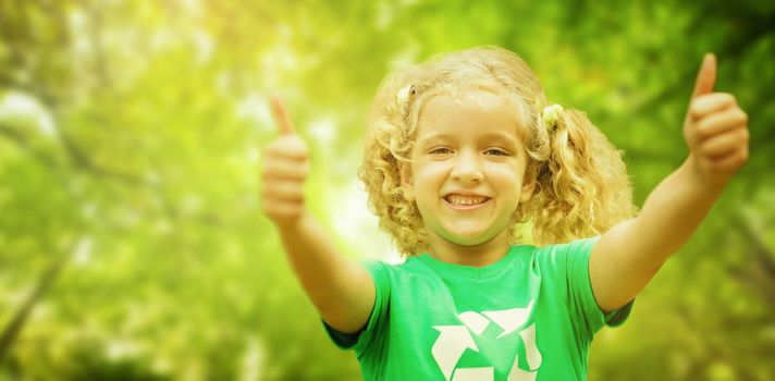 Happy little girl in green with thumbs up  against green leaves