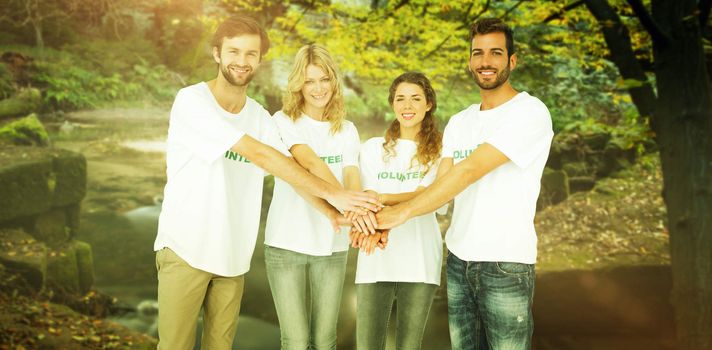 Group portrait of happy volunteers with hands together against rapids flowing along forest