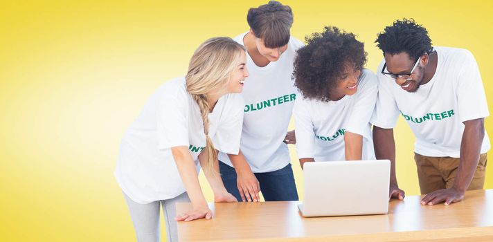 Smiling volunteers working together on a laptop against yellow vignette