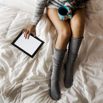 Woman on bed drinking and using a tablet