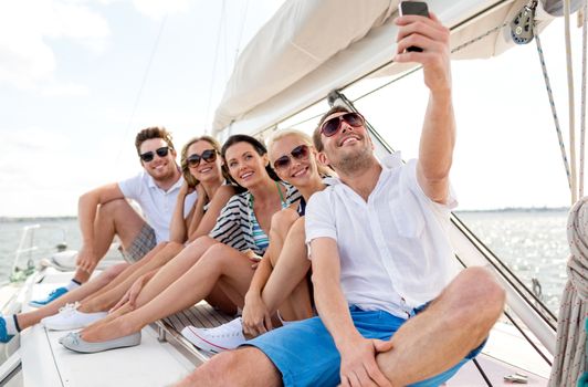 vacation, travel, sea, friendship and people concept - smiling friends sitting on yacht deck and making selfie