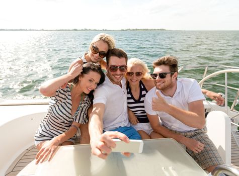 vacation, travel, sea, friendship and people concept - smiling friends sitting on yacht deck and making selfie