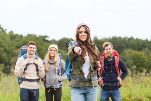 adventure, travel, tourism, hike and people concept - group of smiling friends with backpacks pointing finger outdoors