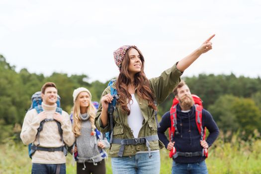 adventure, travel, tourism, hike and people concept - group of smiling friends with backpacks pointing finger outdoors